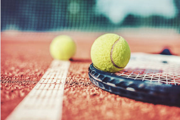 Two tennis balls and a racket resting on the baseline of a clay tennis court