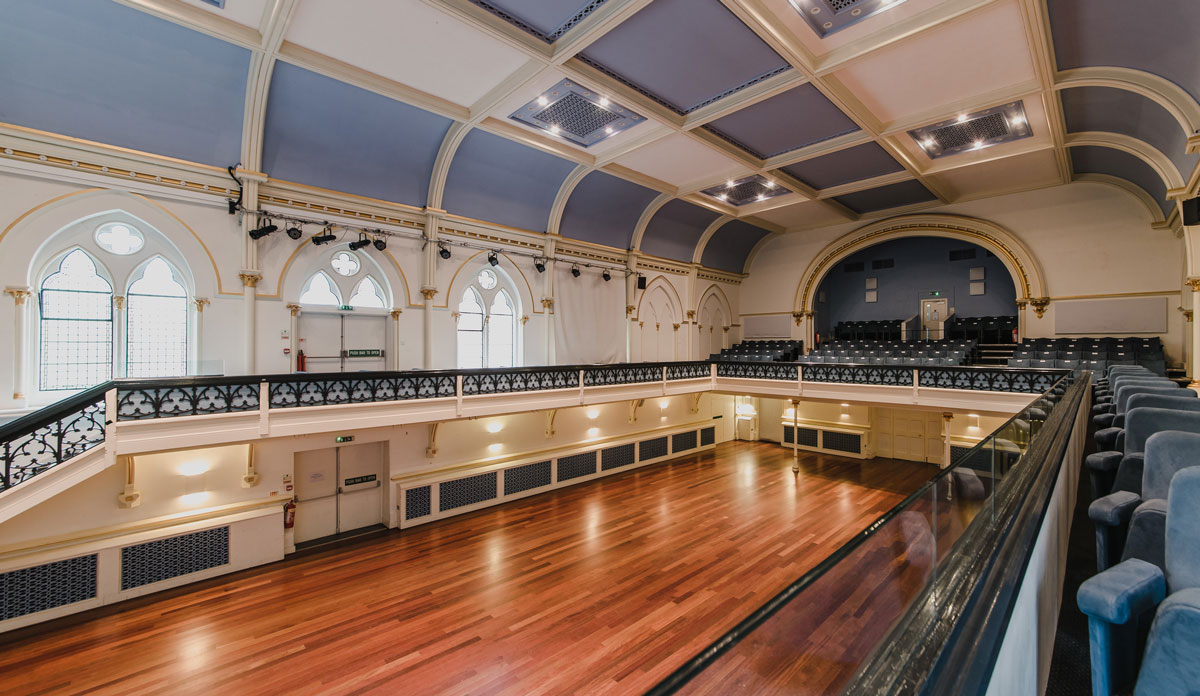 A grand civic hall with a polished wooden floor, vaulted panelled ceiling and tiered balcony seating