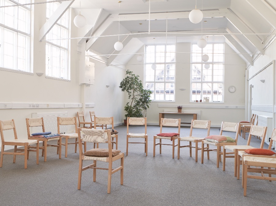 Wooden chairs arranged in a circle in a light meeting room with tall windows