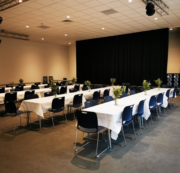 Main Hall — community hall set up with rows of tables, white linen, navy chairs and floral centrepieces in front of a curtained stage
